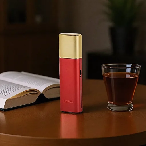Οπτική απεικόνιση του VooPoo Argus Klyc Pod Kit 1300mAh σε χρώμα red-gold πάνω σε ένα τραπέζι με φόντο ένα βιβλίο κι ένα ποτήρι με ουίσκι